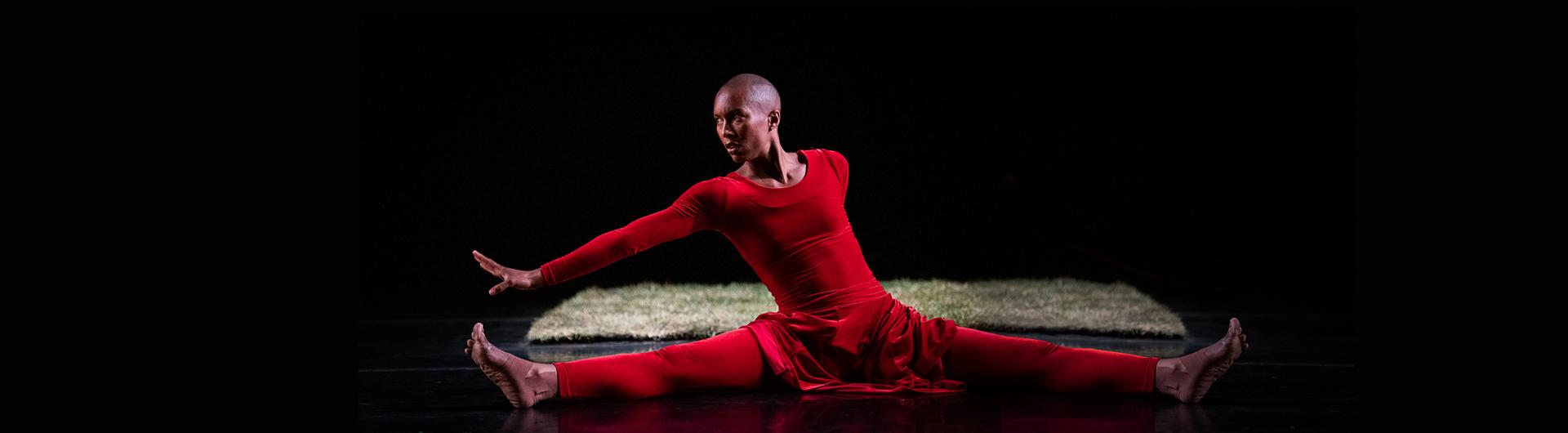 A member of A.I.M by Kyle Abraham on stage. A rectangle of grass can be seen behind the red-clad dancer.