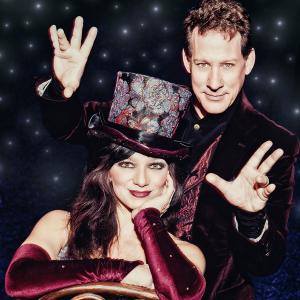 Kalin and Jinger dressed in black. Kalin holds his hands out to either side of Jinger, who wears velvet sleeves and a top hat